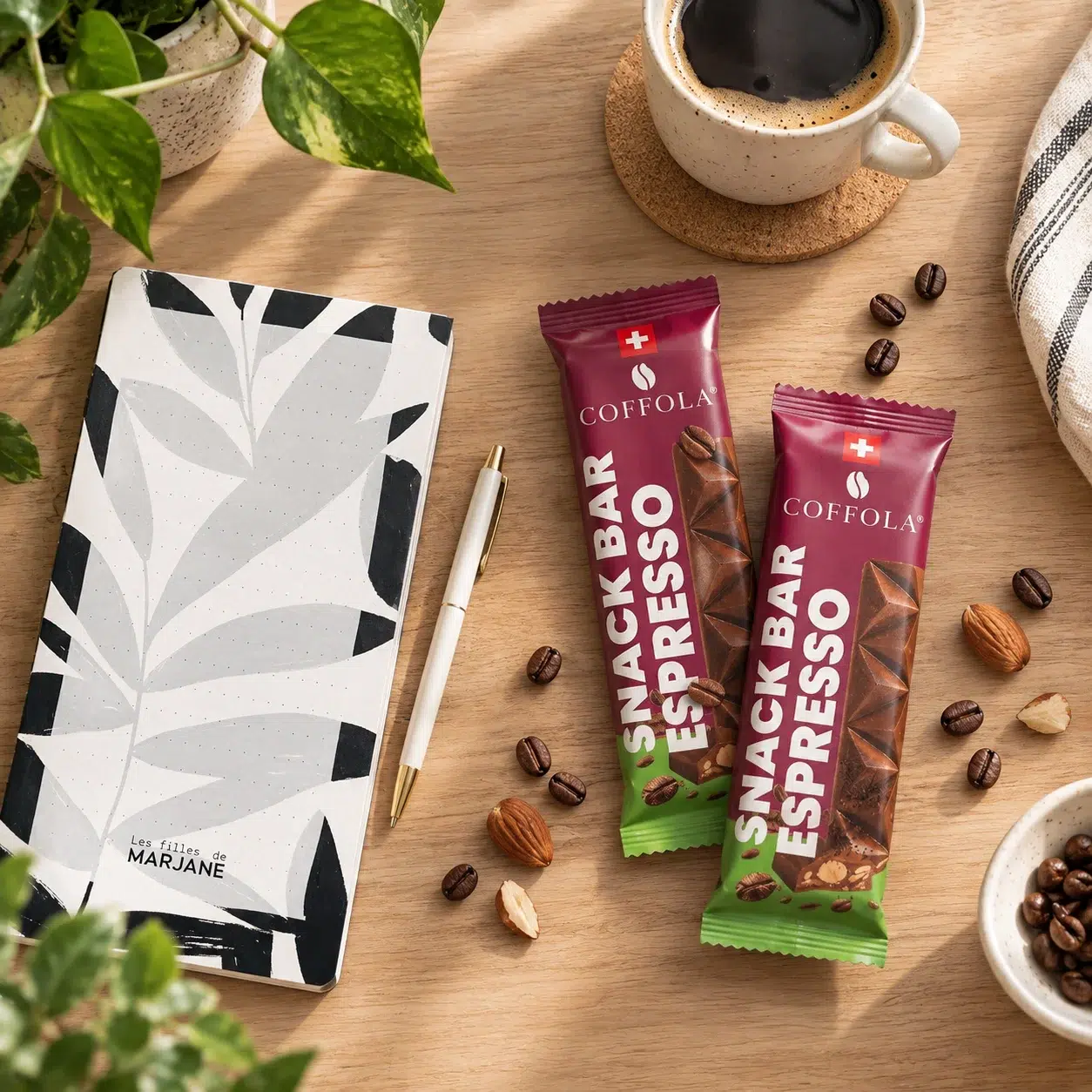 Image présentant les différents produits du Coffret Booste ta rentrée (2 snack bars espresso amandes Coffola, le carnet Les Filles de Marjane) avec une tasse de café